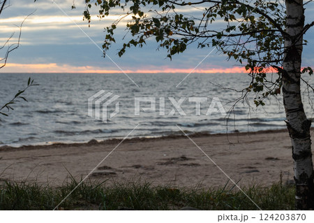 Peaceful scene of a sandy beach at sunset with vibrant hues in the sky. 124203870