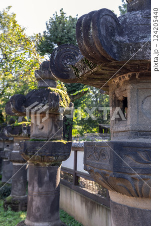 Ancient stone lanterns with carved patterns covered in moss stand near a temple in Japan Ancient stone lanterns with carved patterns covered in moss stand near a temple in Japan 124205440