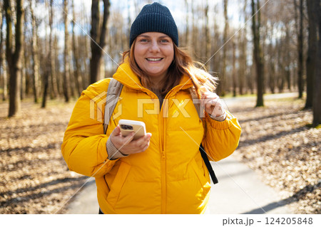 Smiling Woman in Yellow Jacket Walking in the Park Holding a Phone Smiling Woman in Yellow Jacket Walking in the Park Holding a Phone 124205848
