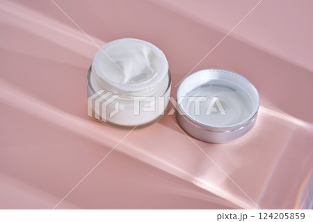 An open jar of cream with its texture on a pink background. 124205859
