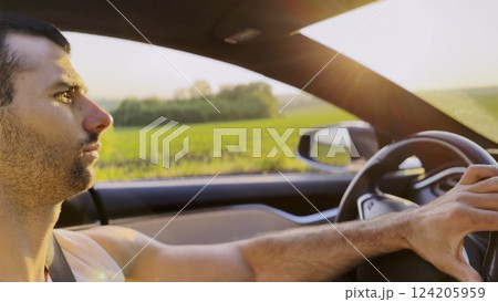 Profile of young handsome man driving a modern electric car with sunlight at background. Young male driver riding on electrical vehicle at countryside. Concept of journey and trip. Close up Profile of young handsome man driving a modern electric car with sunlight at background. Young male driver riding on electrical vehicle at countryside. Concept of journey and trip. Close up 124205959