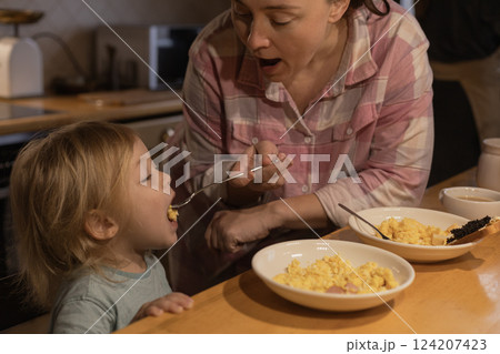 mother feeds her son scrambled eggs with a fork in the kitchen mother feeds her son scrambled eggs with a fork in the kitchen 124207423