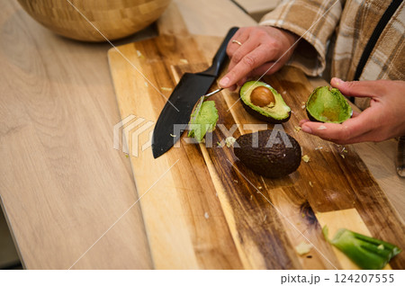 Person Preparing Fresh Avocado on a Wooden Cutting Board 124207555