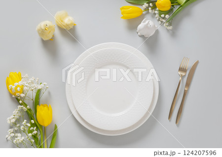 Easter table setting with spring yellow tulips, white plates, bunny, eggs on gray background. Happy Easter celebration. Copy space. View from above. 124207596