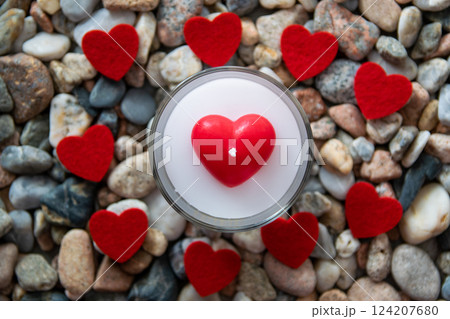 Romantic candle and red bright fabric hearts on other stones near the river. Romantic candle and red bright fabric hearts on other stones near the river. 124207680