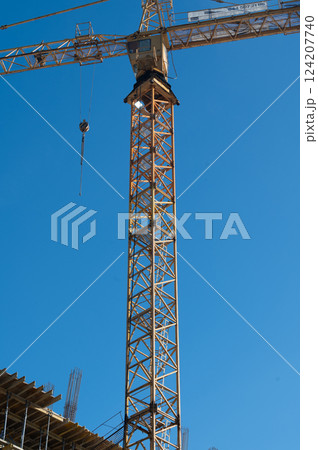 Construction crane reaches new heights against a clear blue sky with a bustling construction site below, symbolizing progress and development in urban settings 124207740