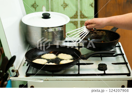 Perfectly golden crispy fritters sizzle on the stove as a skilled hand uses a spatula to expertly flip each piece in a cozy kitchen at midday Perfectly golden crispy fritters sizzle on the stove as a skilled hand uses a spatula to expertly flip each piece in a cozy kitchen at midday 124207908