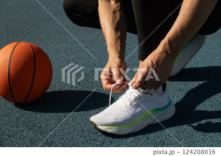 Basketball player tying sports shoes in court outdoors. Last preparation. Team game. Close up 124208016