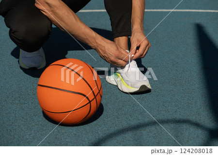 Close up basketball player tying sports shoes in basketball court outdoors. Last preparation. Team game. Close up basketball player tying sports shoes in basketball court outdoors. Last preparation. Team game. 124208018