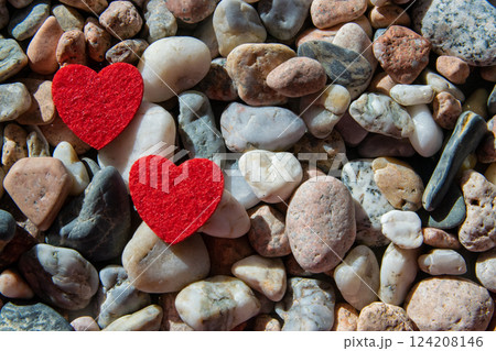 Two red bright fabric heart on other stones near the river. Romantic background. Two red bright fabric heart on other stones near the river. Romantic background. 124208146