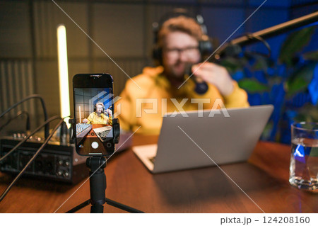 Live streaming with smiling millennial man as radio presenter with microphone, talk show or entertainment. Male person content creator and happy on podcast host in studio for recording audio or social Live streaming with smiling millennial man as radio presenter with microphone, talk show or entertainment. Male person content creator and happy on podcast host in studio for recording audio or social 124208160