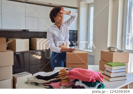 people, moving new place and repair concept - happy african american young woman with many cardboard boxes sitting on floor at home 124208304
