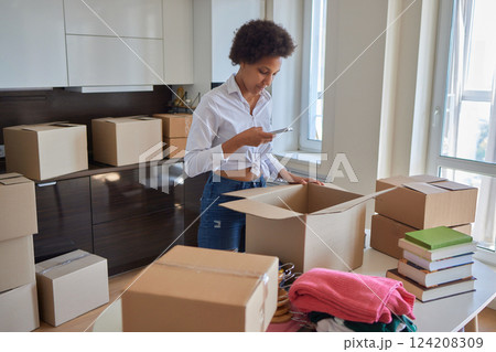 people, moving new place and repair concept - happy african american young woman with many cardboard boxes sitting on floor at home 124208309