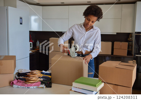 people, moving new place and repair concept - happy african american young woman with many cardboard boxes sitting on floor at home 124208311
