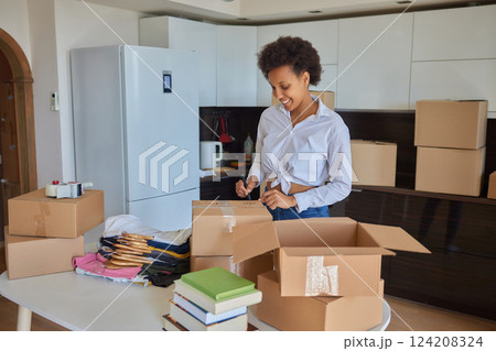 people, moving new place and repair concept - happy african american young woman with many cardboard boxes sitting on floor at home 124208324