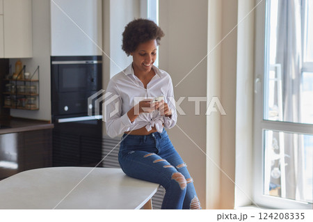 Mobile Application. Relaxed Black Woman Using App On Smartphone At Modern Kitchen Interior 124208335