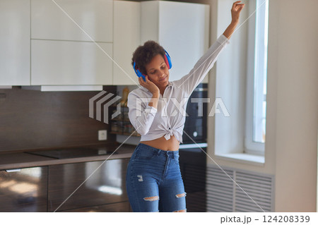 Overjoyed millennial girl wearing headphones have fun moving listening to music relax in living room, happy young woman in earphones dance enjoy leisure weekend at home, stress free concept 124208339