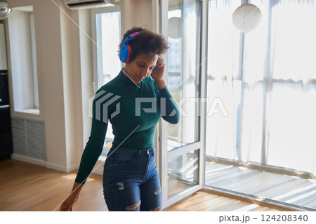 Overjoyed millennial girl wearing headphones have fun moving listening to music relax in living room, happy young woman in earphones dance enjoy leisure weekend at home, stress free concept 124208340