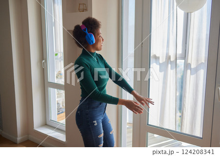 Overjoyed millennial girl wearing headphones have fun moving listening to music relax in living room, happy young woman in earphones dance enjoy leisure weekend at home, stress free concept 124208341