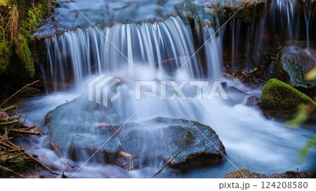 Gentle waterfall cascading over mossy rocks in a serene forest setting during the early morning light 124208580