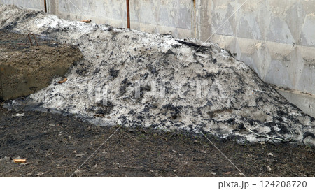 An old snowdrift slowly melting under the warmth of spring reveals a mixture of dirt and debris, resting against an aged wall, marking the transition from winter to warmer days. 124208720