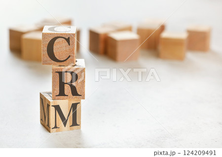 Three wooden cubes with letters CRM (means Customer Relationship Management), on white table, more in background, space for text in right down corner 124209491