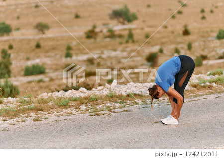Determined Female Athlete Stretching After an Intense Run Through Rugged Mountain Terrain. 124212011