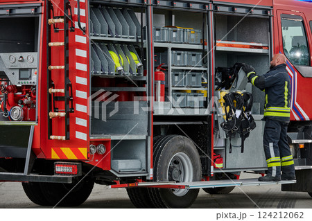 A firefighter meticulously prepares a modern firetruck for a mission to evacuate and respond to dangerous situations, showcasing the utmost dedication to safety and readiness in the face of a fire A firefighter meticulously prepares a modern firetruck for a mission to evacuate and respond to dangerous situations, showcasing the utmost dedication to safety and readiness in the face of a fire 124212062