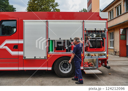 A dedicated firefighter preparing a modern firetruck for deployment to hazardous fire-stricken areas, demonstrating readiness and commitment to emergency response 124212096