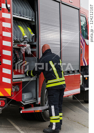 A firefighter meticulously prepares a modern firetruck for a mission to evacuate and respond to dangerous situations, showcasing the utmost dedication to safety and readiness in the face of a fire A firefighter meticulously prepares a modern firetruck for a mission to evacuate and respond to dangerous situations, showcasing the utmost dedication to safety and readiness in the face of a fire 124212107