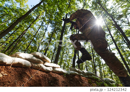 An elite soldier adeptly clears military barriers in the perilous wooded terrain, showcasing tactical skill and agility during specialized training An elite soldier adeptly clears military barriers in the perilous wooded terrain, showcasing tactical skill and agility during specialized training 124212342