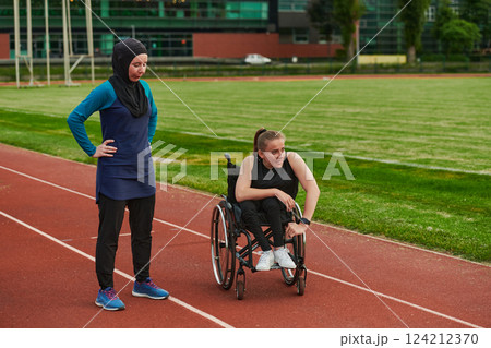 A Muslim woman wearing a burqa resting with a woman with disability after a hard training session on the marathon course 124212370