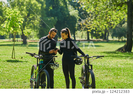 A sweet couple, equipped with bicycles and engrossed in coordinating their journey, checks their GPS mobile and watches while planning scenic routes in the park, seamlessly blending technology and A sweet couple, equipped with bicycles and engrossed in coordinating their journey, checks their GPS mobile and watches while planning scenic routes in the park, seamlessly blending technology and 124212383