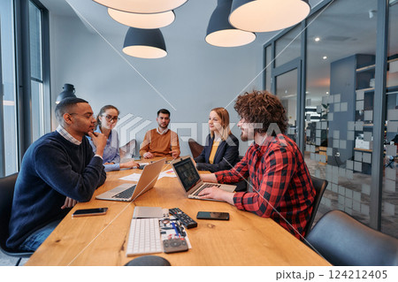 In the vibrant ambiance of a modern startup office, a diverse team of business professionals engage in discussions on various projects and develop new business strategies, epitomizing creativity and 124212405