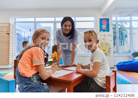Creative kids during an art class in a daycare center or elementary school classroom drawing with female teacher. 124212406