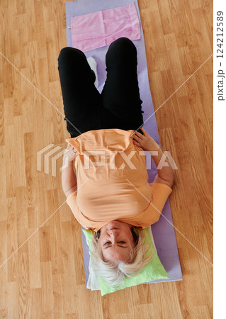 Senior woman practicing stretching and meditation on the floor, focusing on proper alignment and relaxation. 124212589