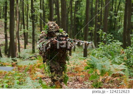 A highly skilled elite sniper, camouflaged in the dense forest, stealthily maneuvers through dangerous woodland terrain on a covert and precise mission 124212623