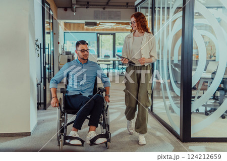 Young business colleagues, collaborative business colleagues, including a person in a wheelchair, walk past a modern glass office corridor, illustrating diversity, teamwork and empowerment in the 124212659