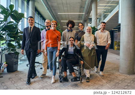 In a spacious and modern startup office, a diverse group of business colleagues, including a colleague in a wheelchair, collaborates and interacts, exemplifying inclusivity, diversity, and teamwork in 124212672