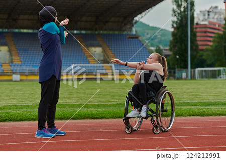 Two strong and inspiring women, one Muslim in a burka and the other in a wheelchair stretching necks while on the marathon course 124212991