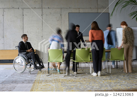A diverse business team, working urgently around a conference table, collaborates on a meeting while their director, seated in a wheelchair, waits for their input A diverse business team, working urgently around a conference table, collaborates on a meeting while their director, seated in a wheelchair, waits for their input 124213063