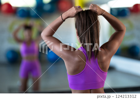 A determined woman ties her hair in preparation for an intense workout, embodying focus and strength as she gears up for her fitness training session A determined woman ties her hair in preparation for an intense workout, embodying focus and strength as she gears up for her fitness training session 124213312