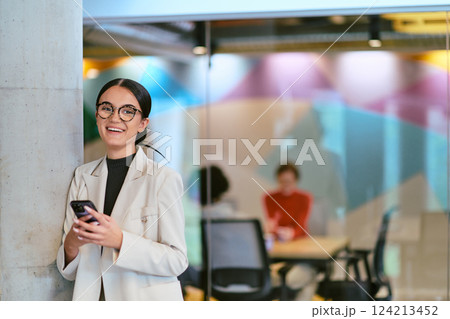 In a modern glass office, a contemporary businesswoman effortlessly multitasks, using her smartphone, while surrounded by colleagues, illustrating the dynamics of corporate life and technology In a modern glass office, a contemporary businesswoman effortlessly multitasks, using her smartphone, while surrounded by colleagues, illustrating the dynamics of corporate life and technology 124213452