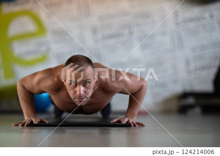 A muscular man performing push ups in the gym, showcasing strength, endurance, and dedication to his fitness routine. A muscular man performing push ups in the gym, showcasing strength, endurance, and dedication to his fitness routine. 124214006