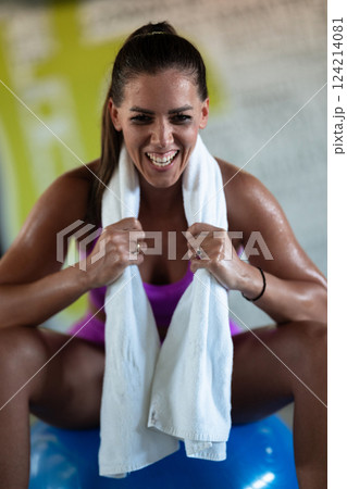 A beautiful and fit woman sitting on a gym ball with a towel, resting and recovering after an intense workout. 124214081