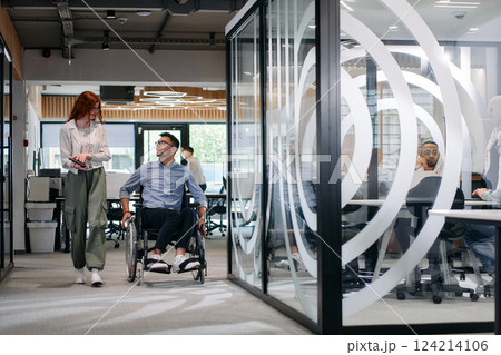 Business colleagues, collaborative business colleagues, including a person in a wheelchair, walk past a modern glass office corridor, illustrating diversity, teamwork and empowerment in the workplace. Business colleagues, collaborative business colleagues, including a person in a wheelchair, walk past a modern glass office corridor, illustrating diversity, teamwork and empowerment in the workplace. 124214106