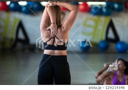 A woman stretches her back and shoulders after an intense fitness workout, focusing on recovery and relieving muscle tension. A woman stretches her back and shoulders after an intense fitness workout, focusing on recovery and relieving muscle tension. 124214346