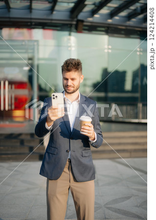 Handsome unshaven businessman walking with laptop, tablet and smartphone on city street 124214408