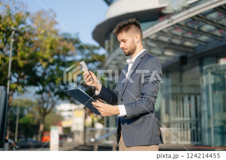 Handsome unshaven businessman walking with laptop, tablet and smartphone on city street 124214455