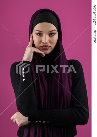 Beautiful Muslim woman in a hijab posing elegantly in a studio with a pink background. 124214656